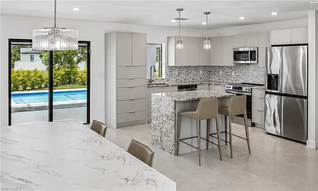 Open-concept kitchen featuring light-toned cabinetry, stainless steel appliances, a multi-tone tile backsplash, and a large central island with seating