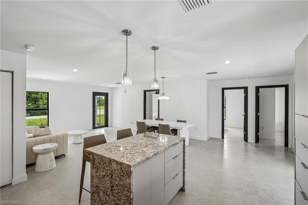 Open-concept living space featuring a kitchen island with stone countertop, recessed lighting, pendant lights, and light-toned flooring
