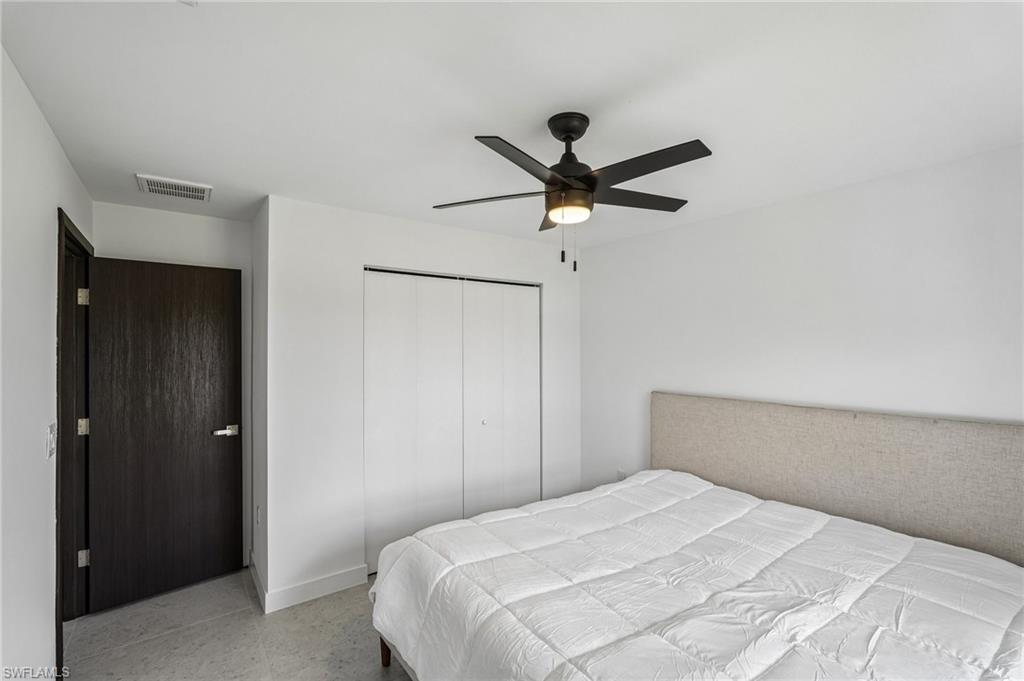Bedroom featuring a dark wood-finish entry door, a ceiling fan with integrated lighting, and a neutral upholstered headboard