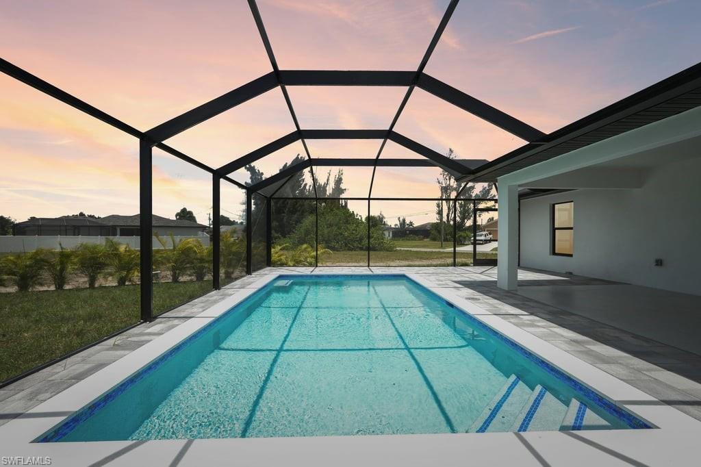 Screened outdoor living area featuring a rectangular swimming pool with integrated steps, surrounded by light-colored pool decking and an expansive covered patio