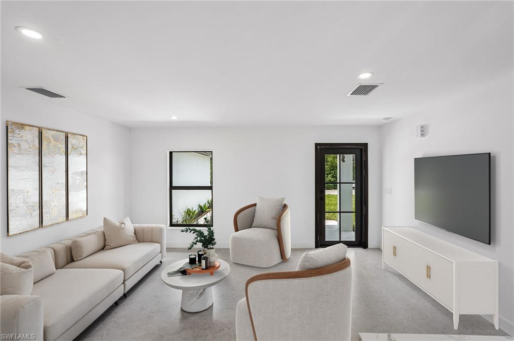 Spacious living area featuring light-colored flooring, recessed lighting, and a dark-framed glass paneled door