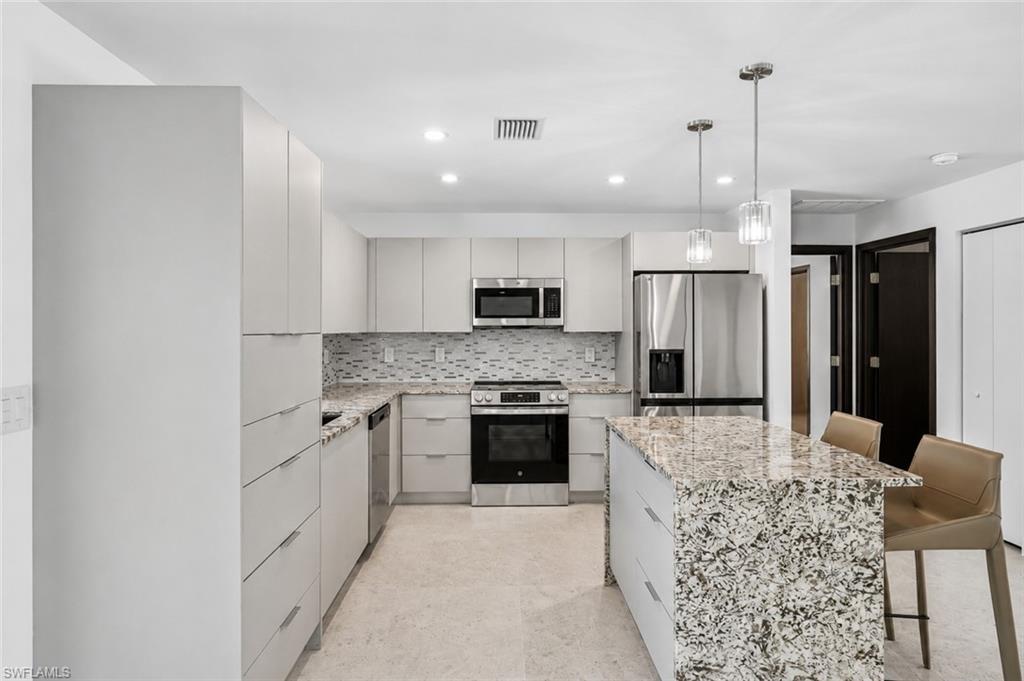 Modern kitchen featuring a central island with a stone countertop, sleek light-toned cabinetry, stainless steel appliances, and a mosaic tile backsplash