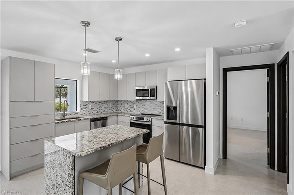 Modern kitchen featuring light cabinetry, stainless steel appliances, a center island with stone countertop, a tile backsplash, and pendant lighting