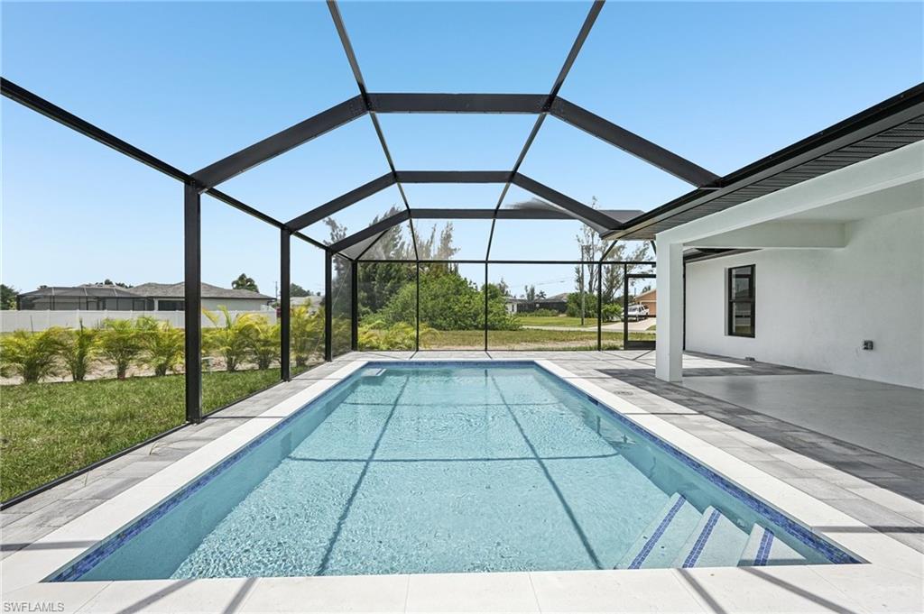 Screened enclosure featuring a rectangular pool with integrated steps, surrounded by light-toned pavers