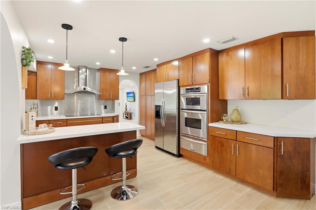 Kitchen with a breakfast bar area, brown cabinets, a peninsula, arched walkways, and decorative light fixtures
