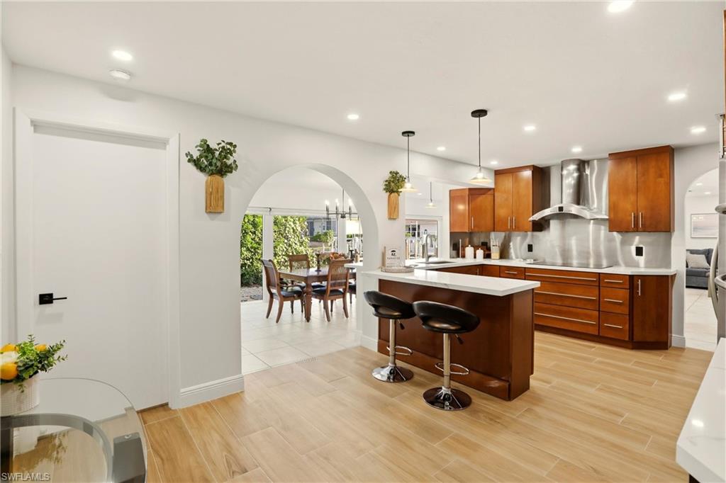Kitchen featuring arched walkways, a breakfast bar, a peninsula, pendant lighting, and wall chimney exhaust hood