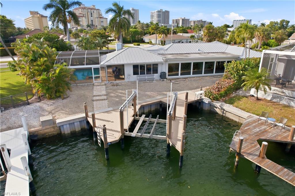 Dock area featuring glass enclosure, a water view, a sunroom, boat lift, and a city view