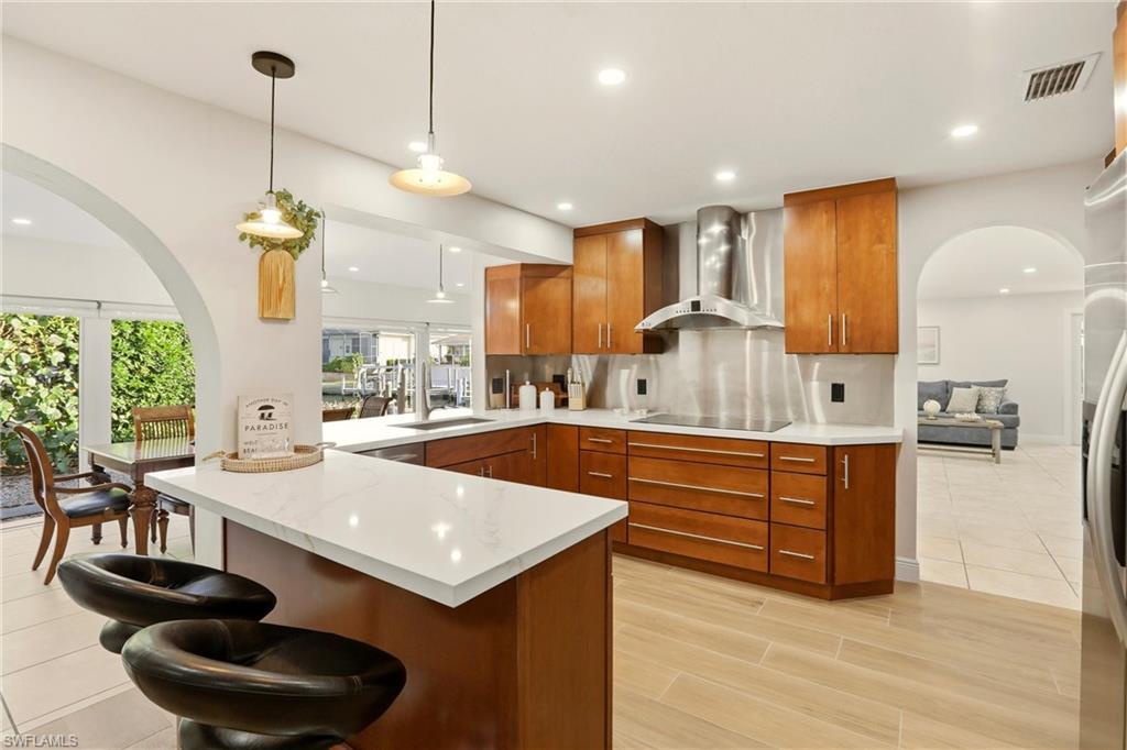 Kitchen featuring arched walkways, a peninsula, brown cabinets, pendant lighting, and a kitchen breakfast bar