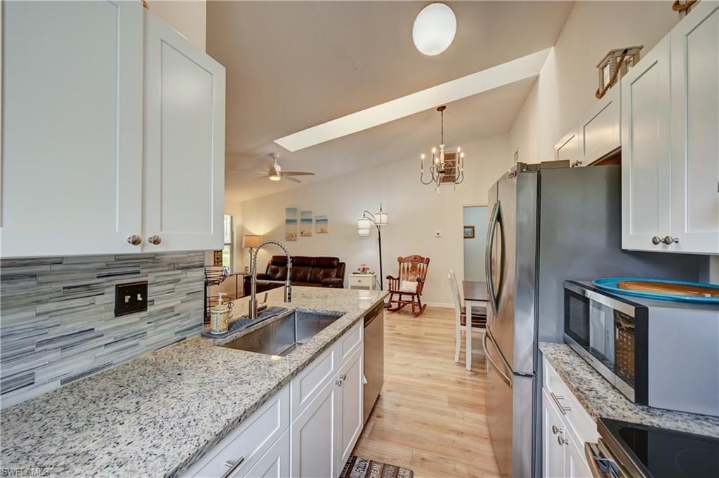 Kitchen with white shaker-style cabinetry, stainless steel sink with gooseneck faucet, light-toned granite-style countertops, and a stacked tile backsplash