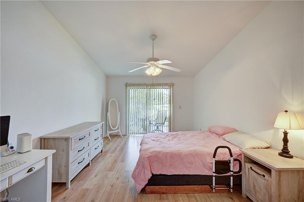 Vaulted ceiling, wood-finish flooring, ceiling fan, sliding glass door, and vertical blinds