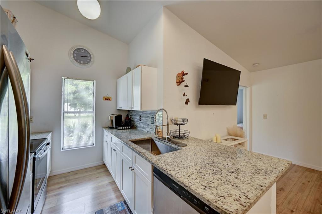 Kitchen featuring granite countertops, wood-finish flooring, stainless steel appliances, white cabinetry, and a tile backsplash