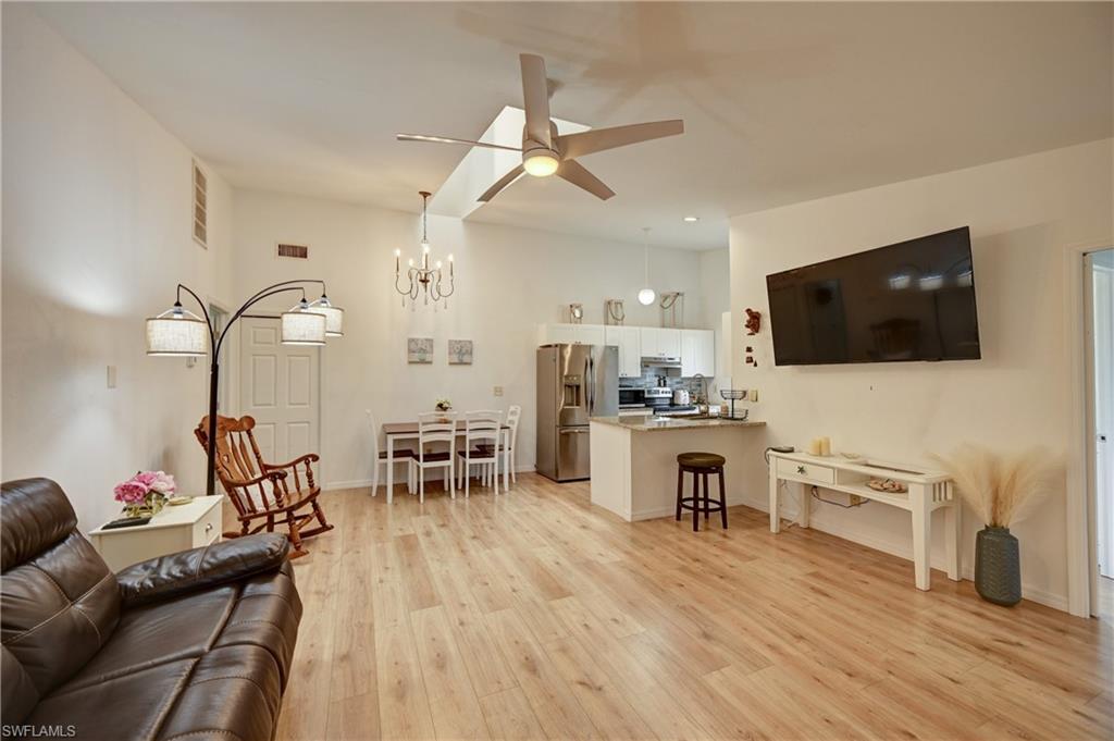 Vaulted ceiling with skylight, wood-finish flooring throughout, ceiling fan with integrated lighting, built-in kitchen cabinetry, and stainless steel appliances