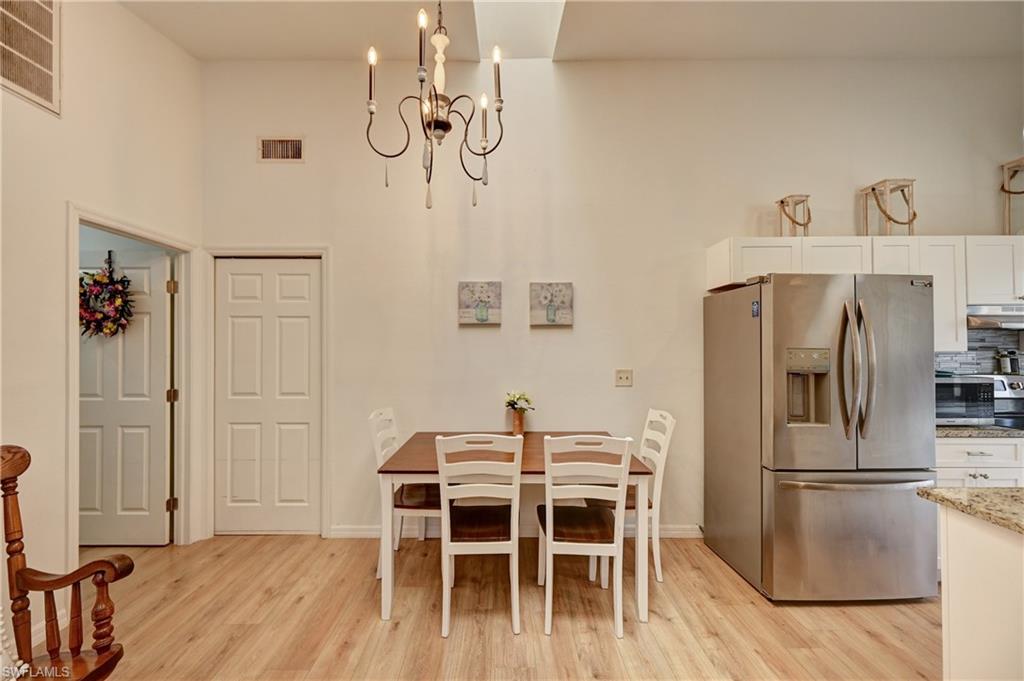 Vaulted ceiling with an attached chandelier, wood-finish flooring, white paneled doors, built-in white cabinetry, and a stainless steel refrigerator