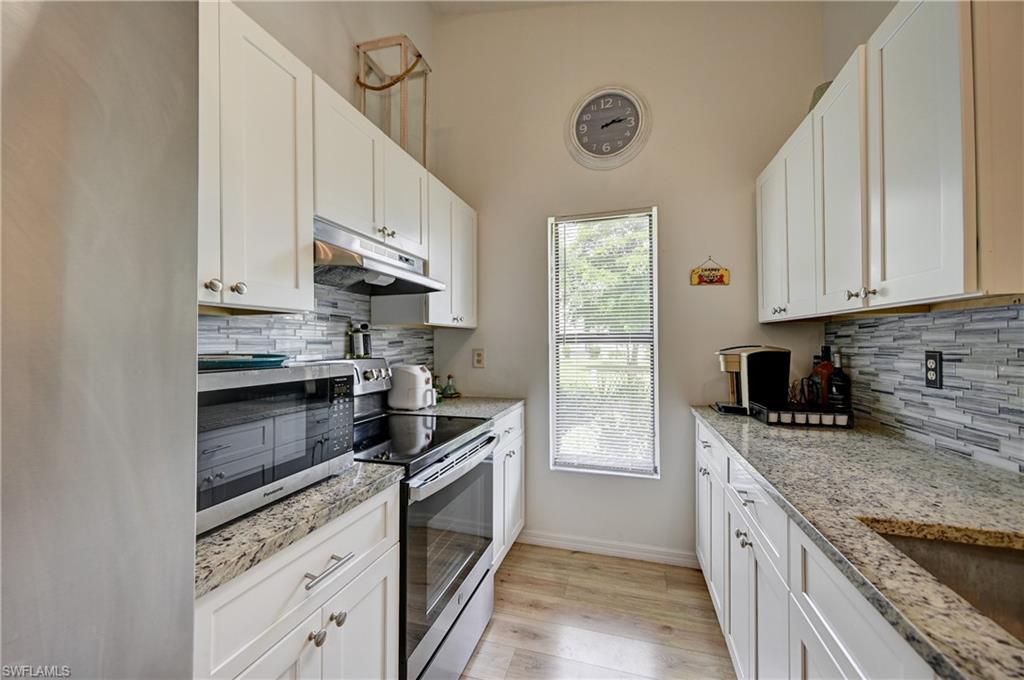 Galley kitchen featuring white cabinetry, light-toned countertops, a glass tile backsplash, and wood-finish flooring