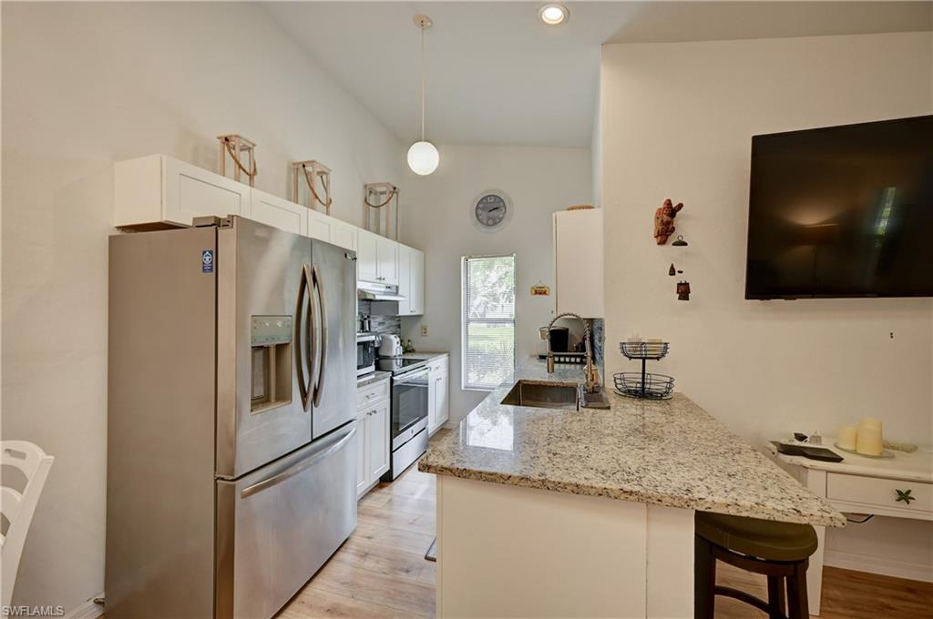 Vaulted ceiling with recessed lighting, stainless steel French door refrigerator, white cabinetry, integrated stainless steel sink, and granite-finish countertops