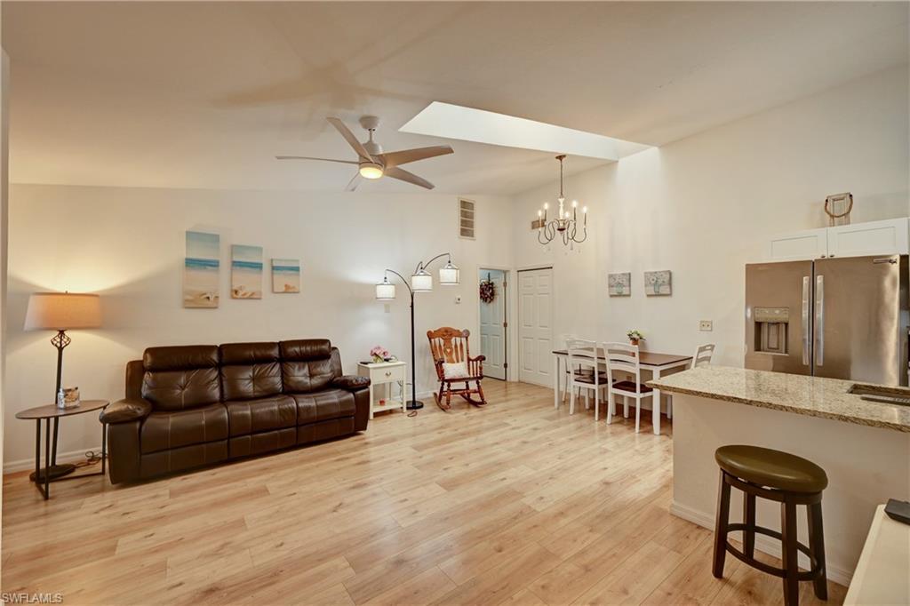 Vaulted ceilings with a skylight and a ceiling fan, wood-finish flooring, a kitchen island with a stone countertop, and stainless steel appliances