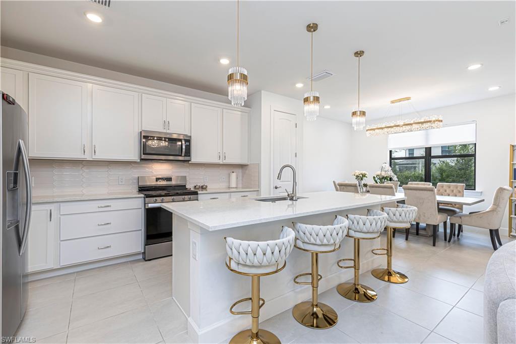 Kitchen featuring stainless steel appliances, a sink, light countertops, backsplash, and an island with sink