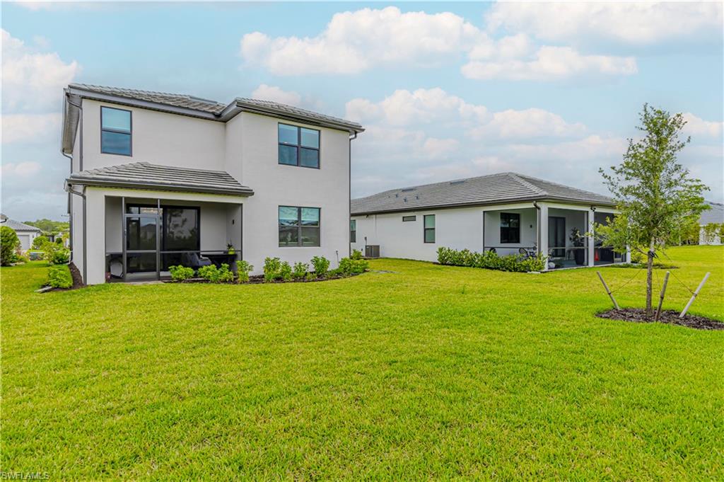 Back of property featuring a sunroom, a yard, stucco siding, a tile roof, and cooling unit
