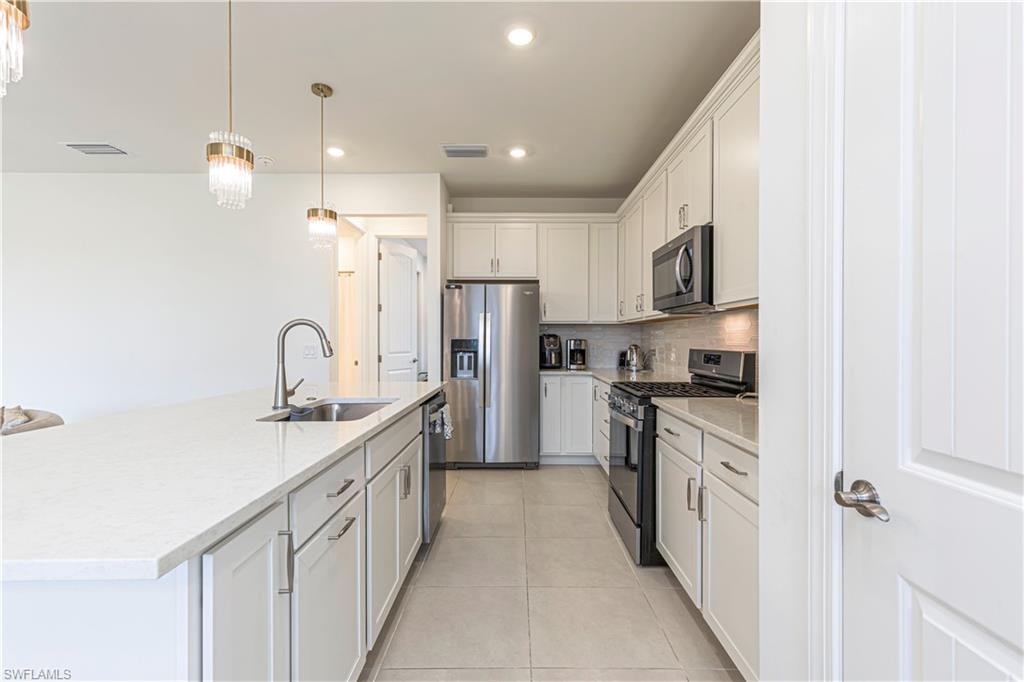 Kitchen with stainless steel appliances, a sink, backsplash, light tile patterned floors, and white cabinetry