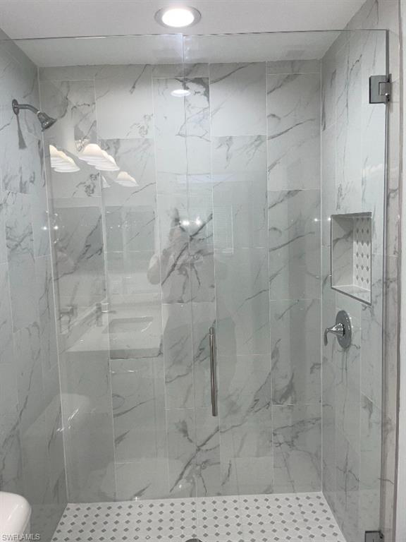 Glass-enclosed shower featuring white and gray marble-look tile, a built-in shower niche, chrome fixtures, and a recessed ceiling light