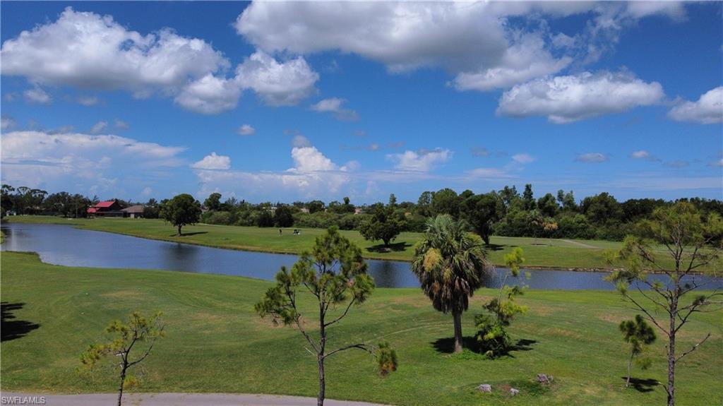 Expansive green space featuring a large body of water, mature trees, and a distant building with a red roof