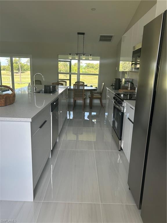 Modern kitchen featuring a large island with a stainless steel sink, sleek white cabinetry, and stainless steel appliances