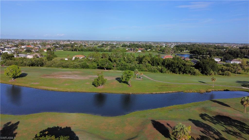 Expansive green space featuring a water hazard, surrounding residential areas, and mature trees under a clear sky