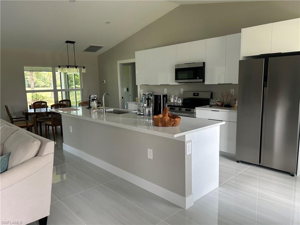 Modern kitchen featuring white cabinetry, stainless steel appliances, a center island with sink, and light-toned tile flooring
