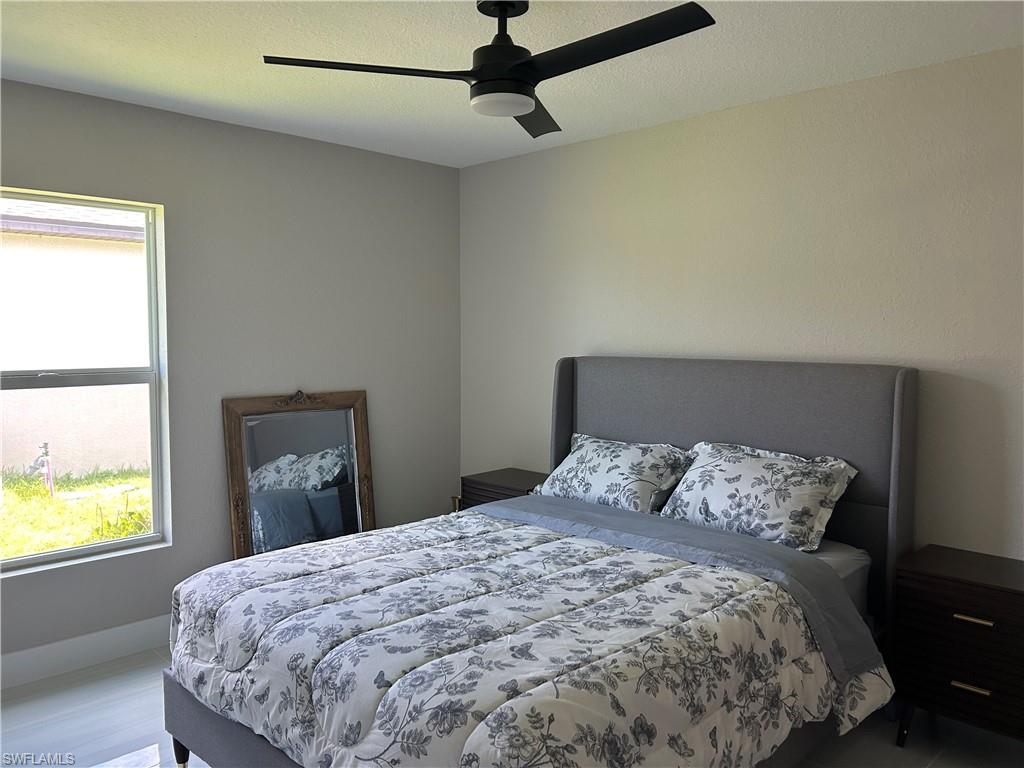 Bedroom featuring a ceiling fan with integrated lighting, a window with a roller shade, and light-toned walls