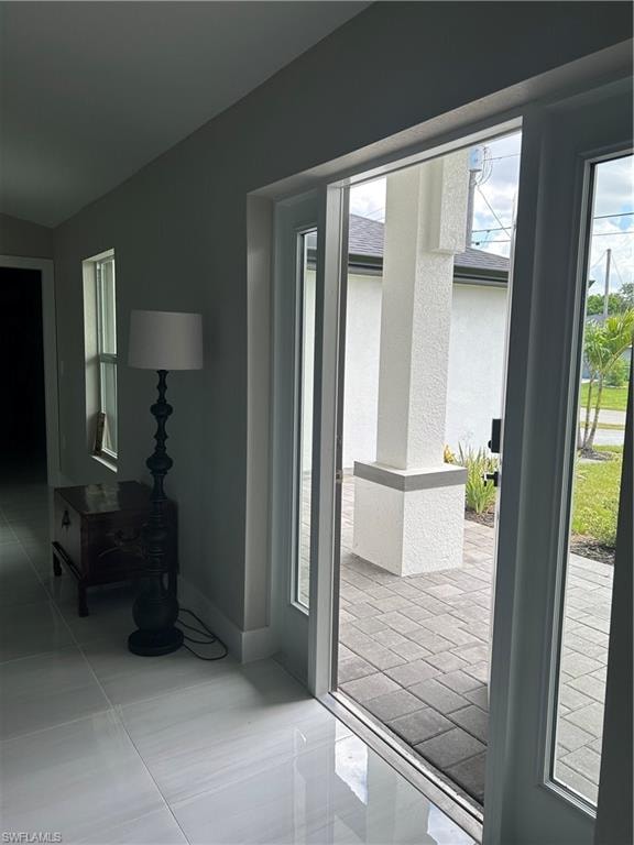 White tile flooring throughout, leading to a front entry with glass panel doors and an exterior paver patio