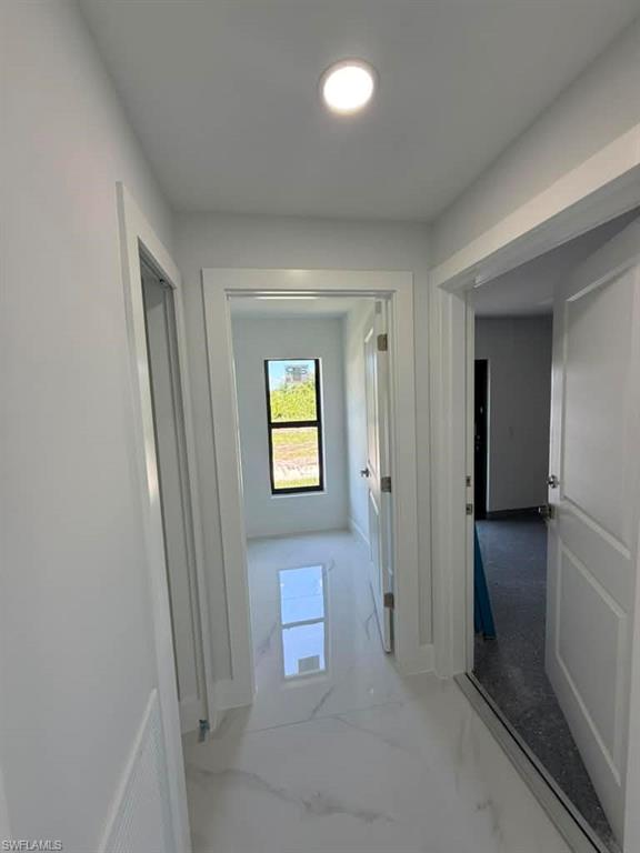Hallway featuring white walls, recessed ceiling lighting, and white tile flooring with grey veining