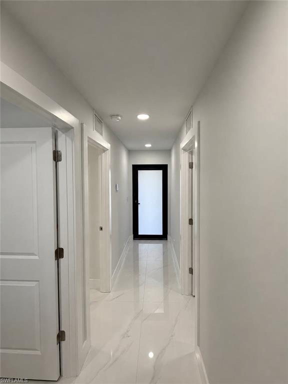 Hallway featuring white marble-look flooring, recessed ceiling lighting, and white baseboards