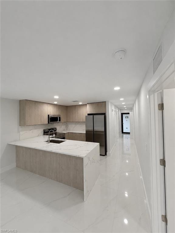 Kitchen featuring light wood-finish cabinetry, stainless steel appliances, a white marble-patterned countertop with integrated sink, and white tile flooring