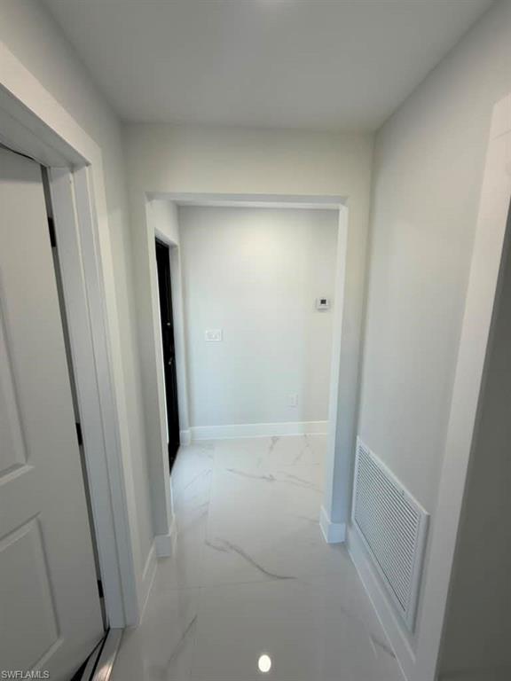 Hallway featuring white paint, white trim, and white tile flooring with subtle veining