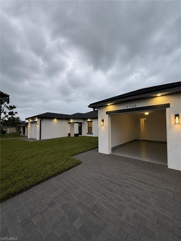 Contemporary exterior featuring a paver driveway, manicured lawn, and exterior lighting