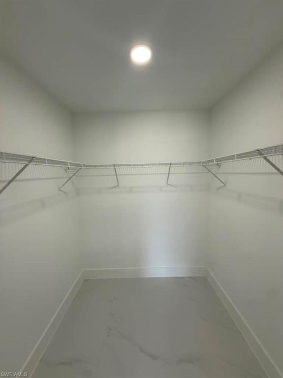 Spacious walk-in closet featuring white wire shelving, recessed lighting, white baseboards, and light-toned tile flooring with subtle veining