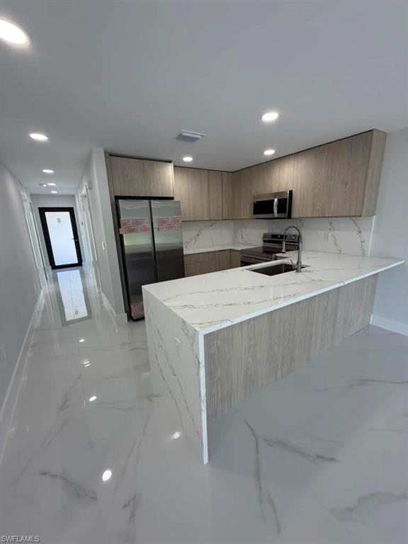 Modern kitchen featuring a waterfall island with a stone-finish countertop, wood-finish cabinetry, stainless steel appliances, and recessed lighting