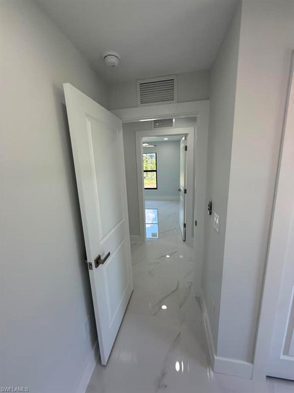 Hallway featuring large format marble-look tile flooring, white interior doors with dark hardware, and clean white baseboards