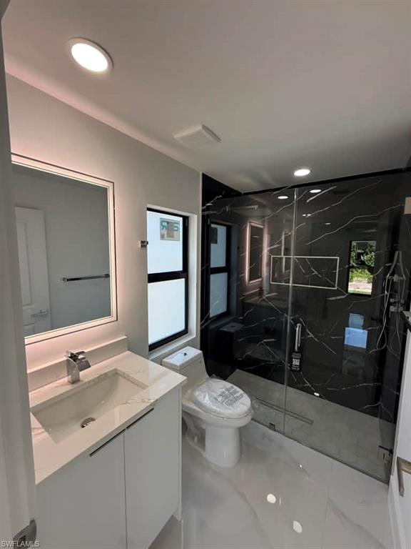 Bathroom featuring a glass-enclosed shower with black marble-effect wall tiles, a white vanity with a rectangular undermount sink, a chrome faucet, and a lighted mirror