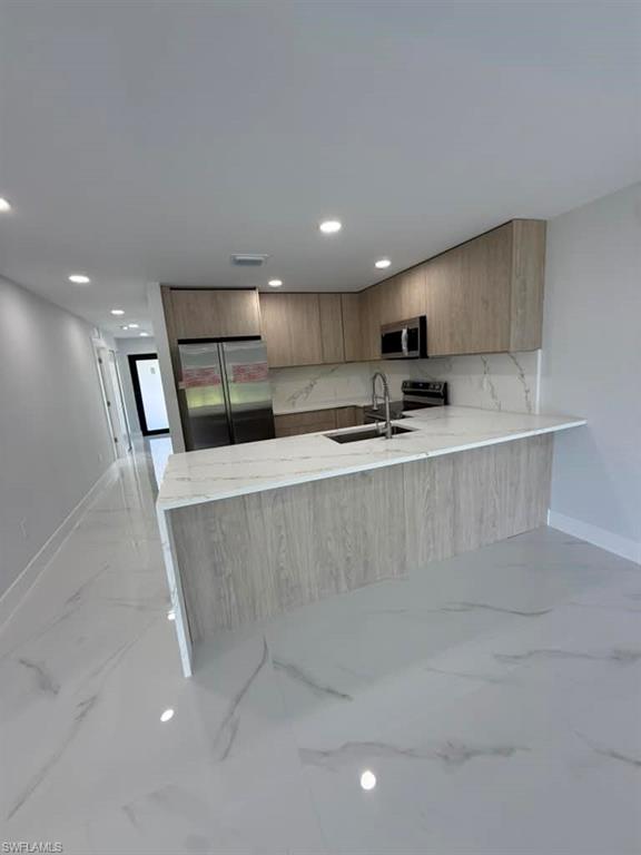 Contemporary kitchen featuring light wood-finish cabinetry, stainless steel appliances, and white countertops with gray veining