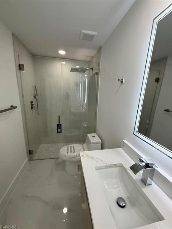 Contemporary bathroom featuring a frameless glass shower enclosure, a rainfall showerhead, a modern vanity with integrated sink, a rectangular illuminated mirror, and large format tile flooring