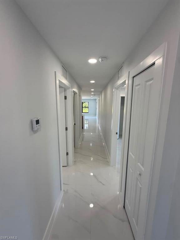 Long hallway featuring white tile flooring with gray veining, white baseboards, and white walls