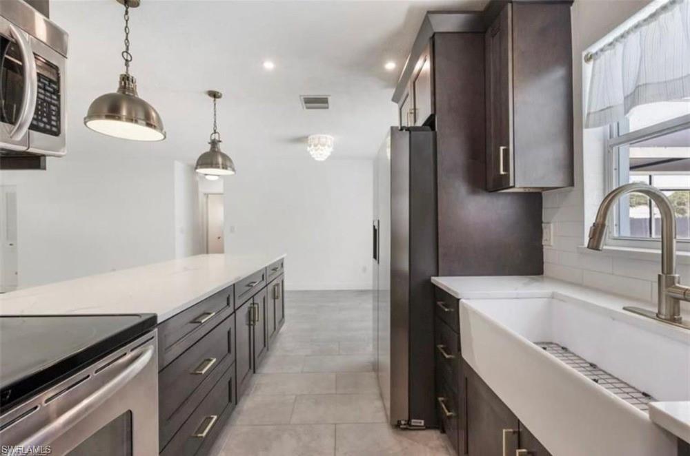 Modern kitchen featuring dark wood cabinetry, stainless steel appliances, a large center island with a light-toned countertop, a farmhouse sink, and contemporary pendant lighting