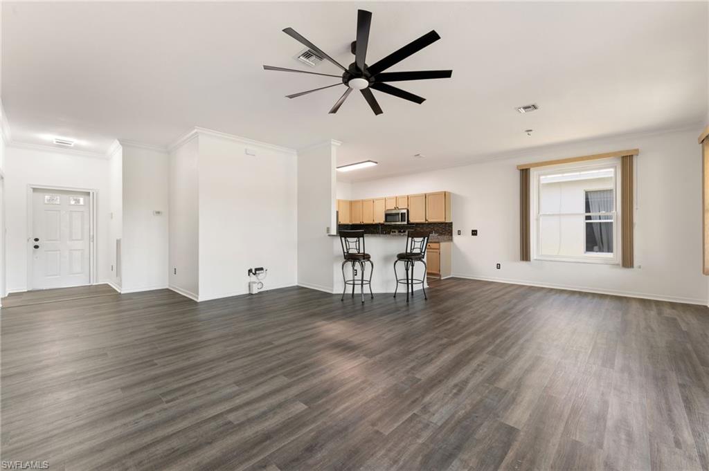 Spacious room featuring wood-finish flooring, a contemporary ceiling fan, and a kitchen alcove with light wood cabinetry and dark countertops