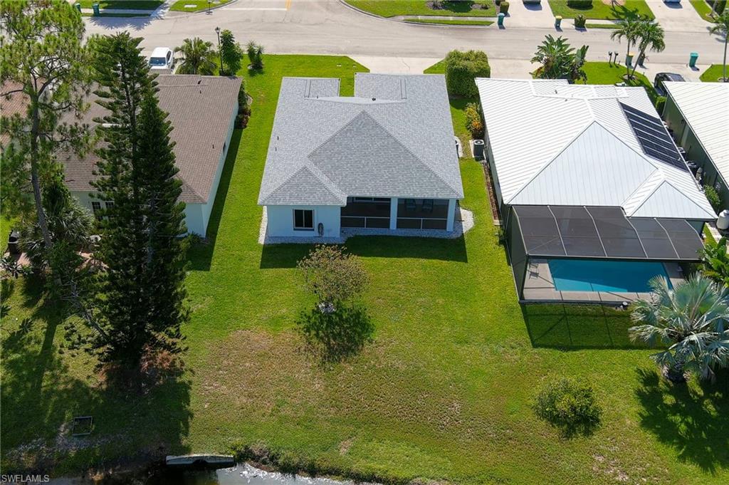 Rear exterior featuring a screened lanai with a concrete patio, a private dock, and mature landscaping