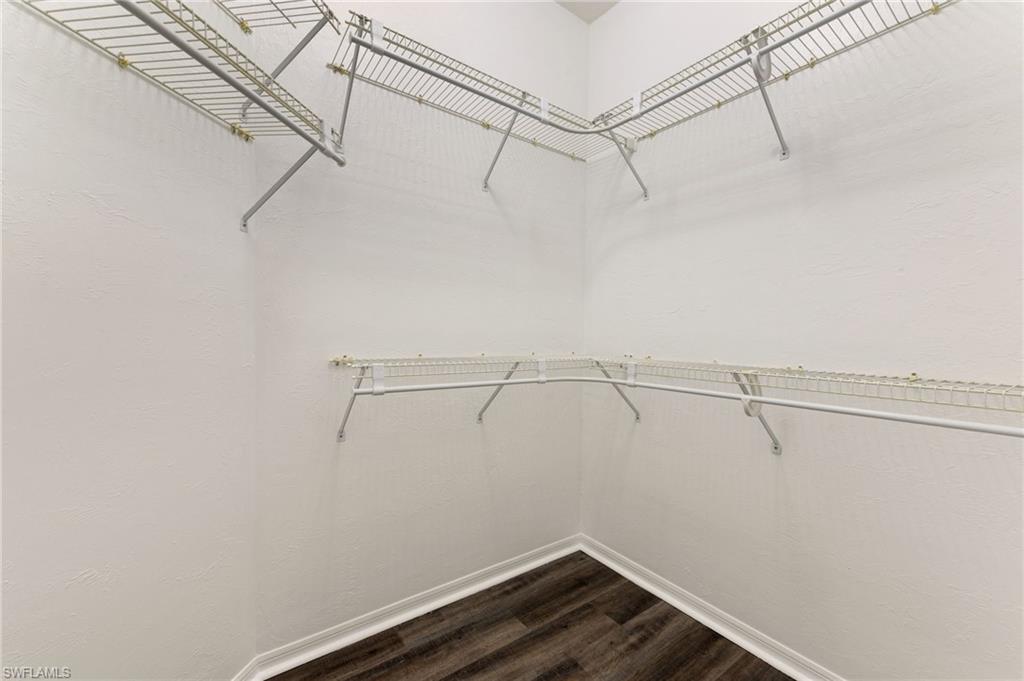 Walk-in closet featuring white wire shelving, hanging rods, white baseboards, and wood-finish flooring