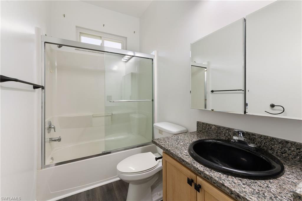 Full bathroom featuring a granite-style countertop with an oval black sink, a light wood-finish vanity, and a shower-tub combination with sliding glass doors