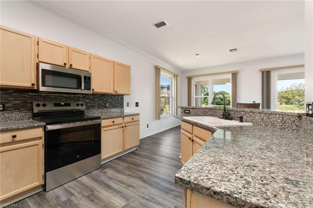 Kitchen featuring light wood cabinetry, stainless steel appliances, granite countertops, and a mosaic tile backsplash