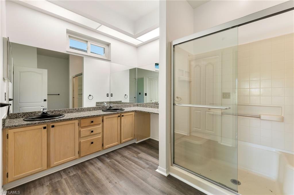 Bathroom featuring wood-finish flooring, a double vanity with stone countertops and undermount sinks, an extended mirror, and a glass-enclosed shower with tiled walls