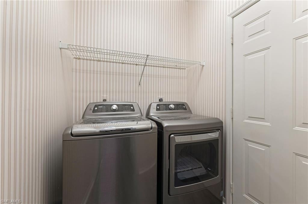 Dedicated laundry space featuring a side-by-side washer and dryer, striped wall covering, and a wire shelving unit